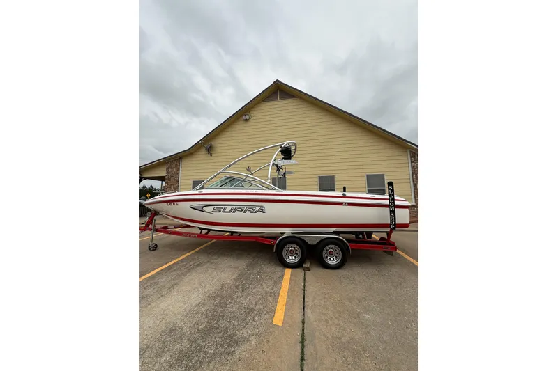 The Image of 2005 Supra Sunsport 24 V boat on trailer, parked near a building. - 1