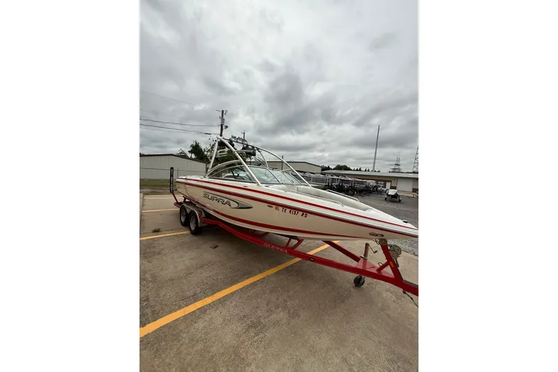 Slide: The Image of 2005 Supra Sunsport 24 V boat on trailer, parked outdoors under cloudy sky. - 2