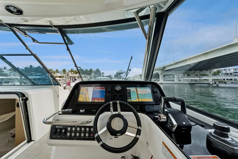 Slide: The Image of Helm of 2025 Aquila 36 Cruiser with navigation screens, steering wheel, and waterfront view. - 30
