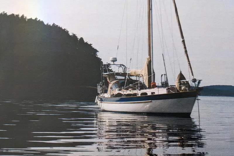 Slide: The Image of 1983 Valiant Cutter sailboat anchored on calm water near forested shoreline. - 24