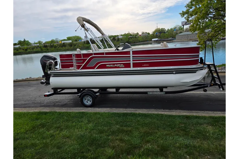 The Image of 2018 Ranger Reata 200F pontoon boat on trailer by a lakeside road. - 0