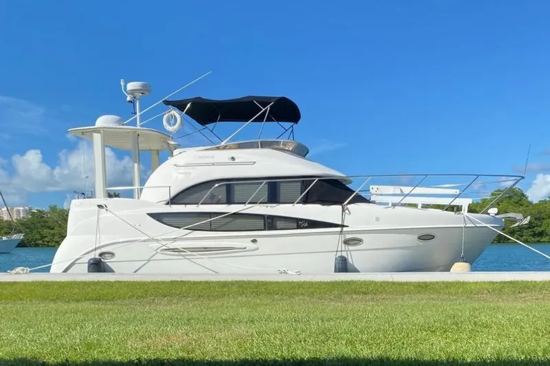 The Image of 2005 Meridian 368 Motoryacht docked by a grassy shore under a clear blue sky. - 0