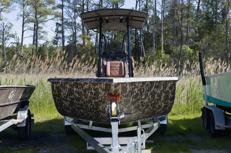 Slide: The Image of Avid 22 Recon 2026 boat with camouflage design on a trailer in a wooded area. - 2