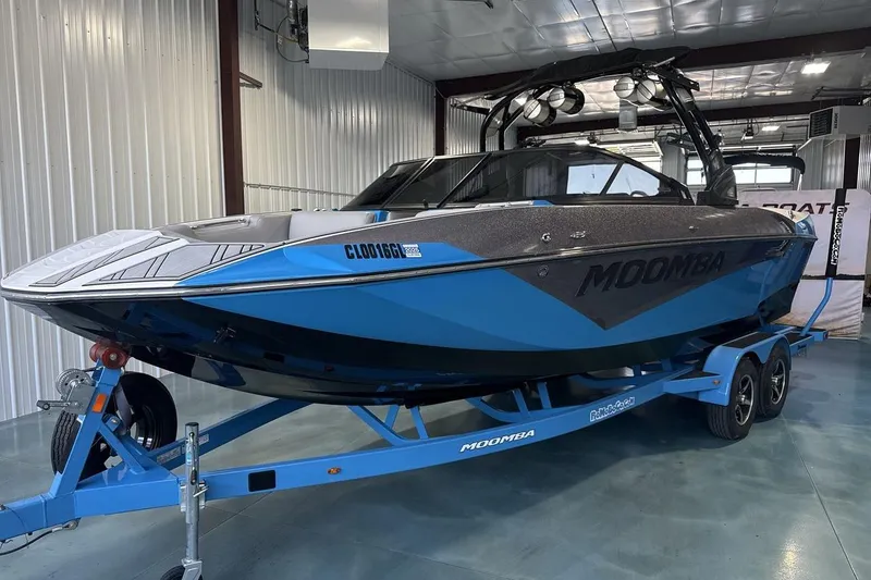 The Image of 2019 Moomba Makai boat in a garage, blue and black design on trailer. - 1