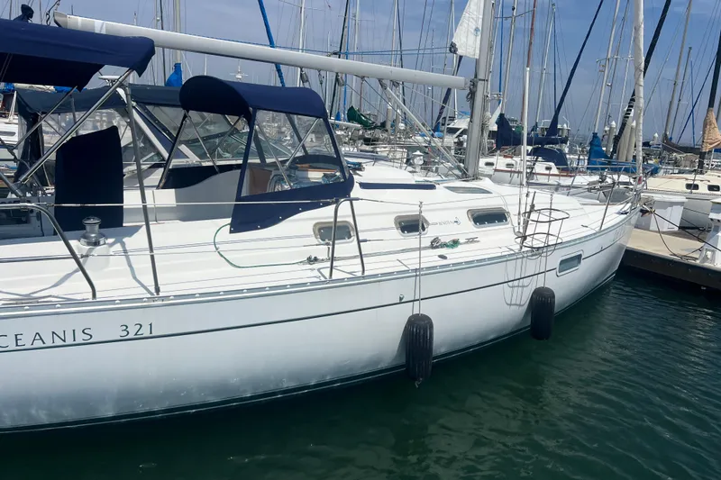 Slide: The Image of 1999 Beneteau Oceanis 321 sailboat docked in a marina, featuring sleek design and blue canopy. - 36