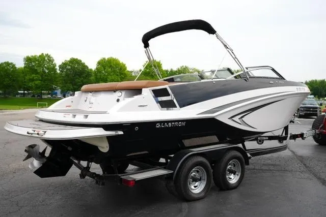 Slide: The Image of 2017 Glastron GT 245 boat on trailer, parked outdoors with green trees in background. - 5