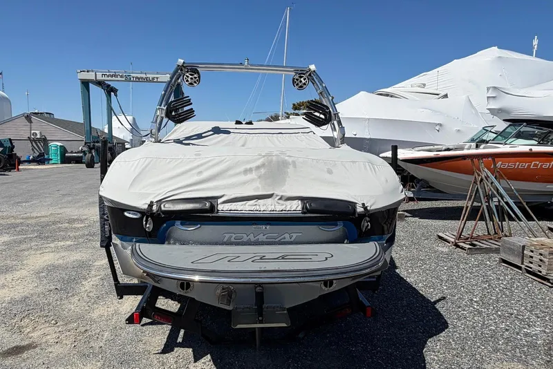 Slide: The Image of 2015 TomCat MB Sports Wake 22 boat covered, parked in a marina with other boats. - 2