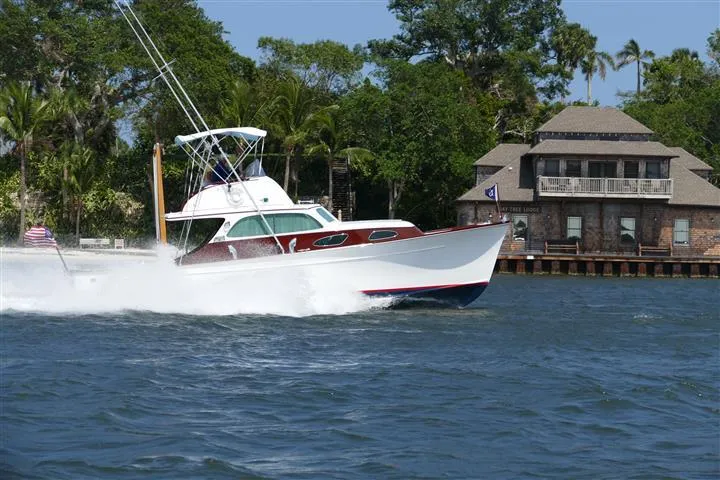 Slide: The Image of 1949 Rybovich Sport Fish boat cruising on a scenic waterway near a waterfront house. - 2