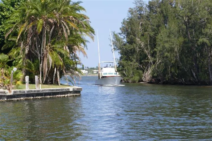 Slide: The Image of 1949 Rybovich Sport Fish boat navigating a scenic, tree-lined waterway. - 6