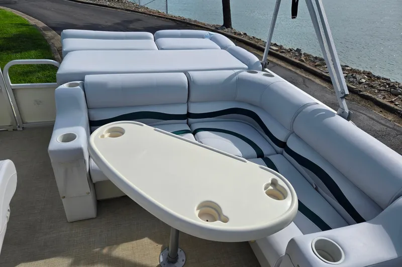 Slide: The Image of 1999 Bennington 2275LX pontoon boat interior with cushioned seating and table by the water. - 13
