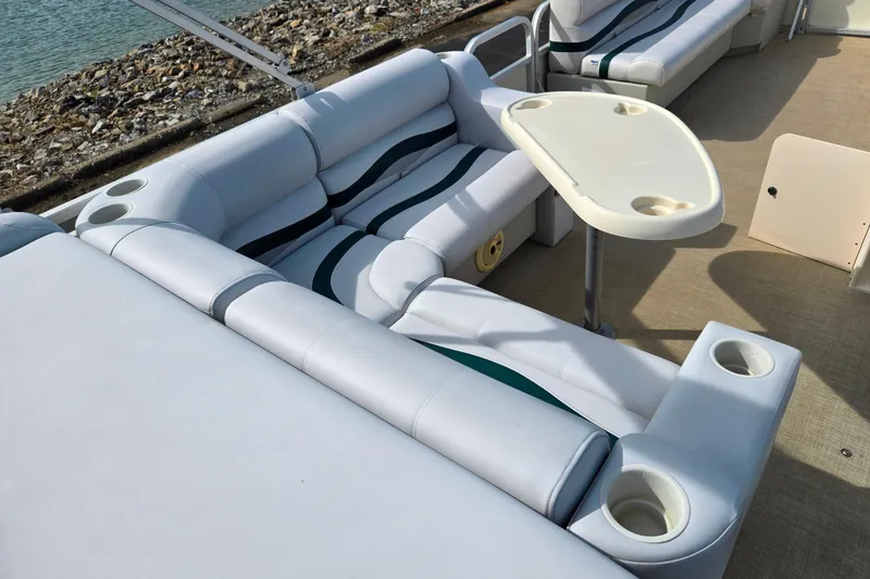 Slide: The Image of Bennington 2275LX 1999 pontoon boat interior with white seating and table by the water. - 19