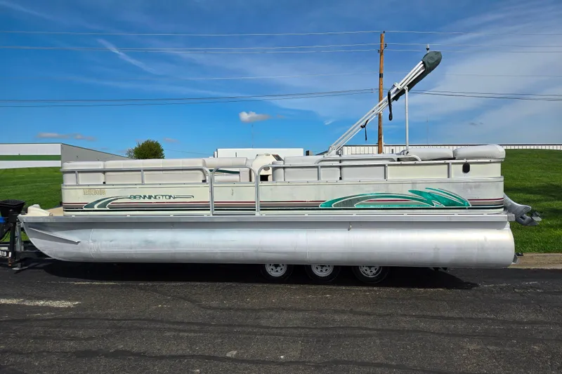 Slide: The Image of 1999 Bennington 2275LX pontoon boat parked on a trailer under a clear blue sky. - 4