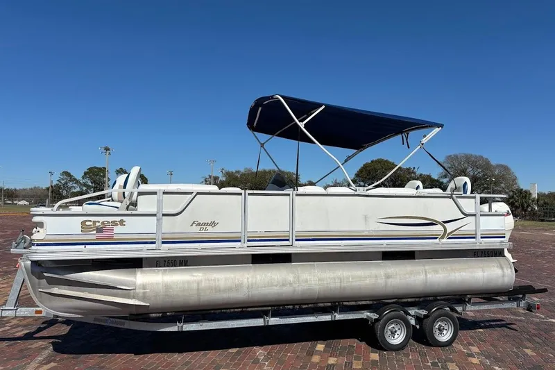 The Image of 2004 Crest 2200 Family DL pontoon boat on trailer, featuring blue canopy and white exterior. - 1