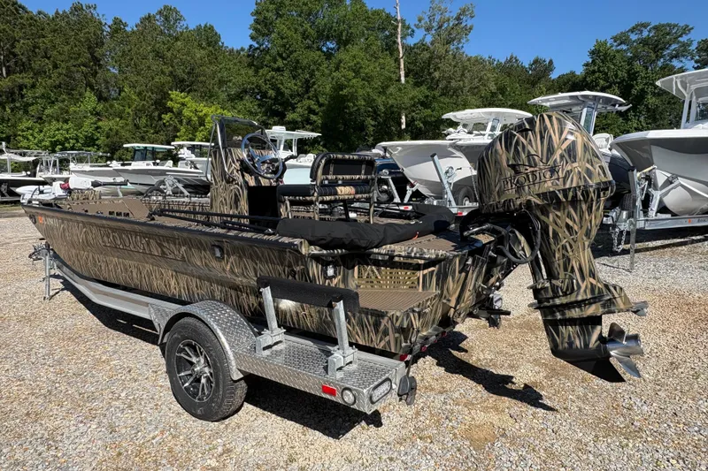 Slide: The Image of 2022 Prodigy 18' PRO VS boat with camouflage design on a trailer, surrounded by trees and other boats. - 5