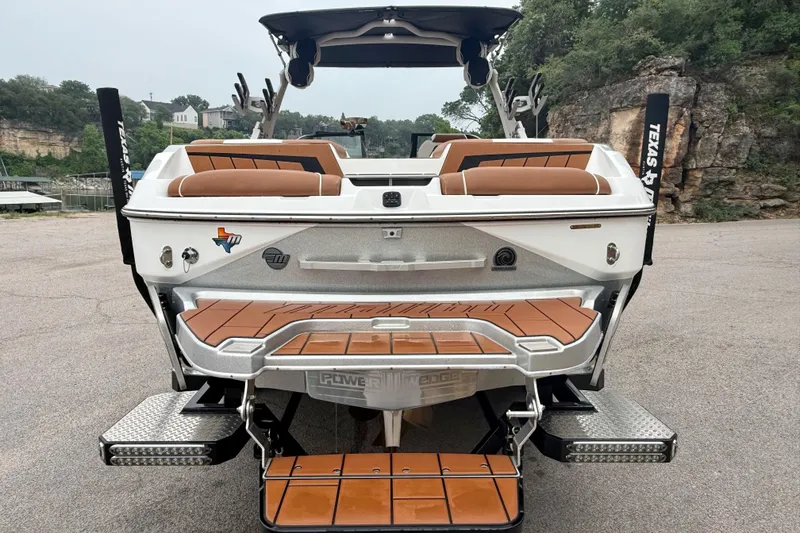 Slide: The Image of 2023 Malibu Wakesetter 24 MXZ boat with brown seating and swim platform, parked outdoors. - 11