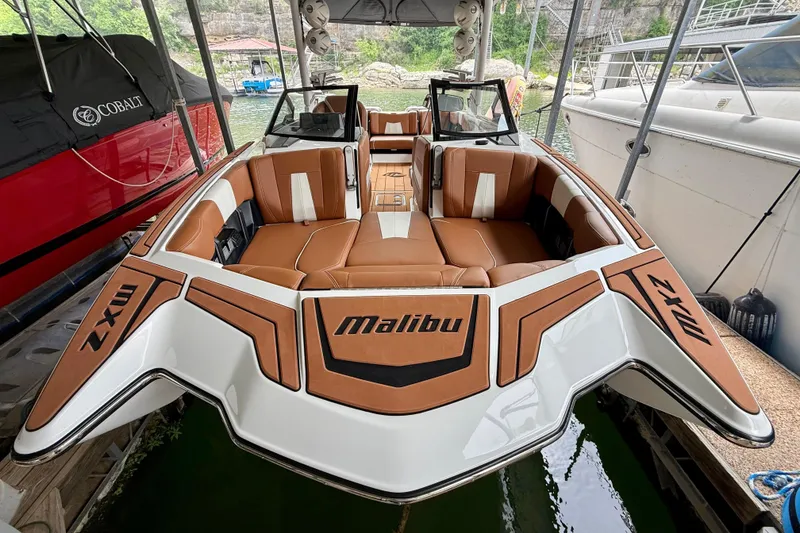 Slide: The Image of 2023 Malibu Wakesetter 24 MXZ boat with luxurious brown seating, docked in a marina. - 15