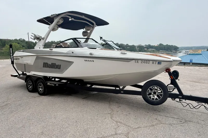 Slide: The Image of 2023 Malibu Wakesetter 24 MXZ boat on trailer, parked near a lake. - 8