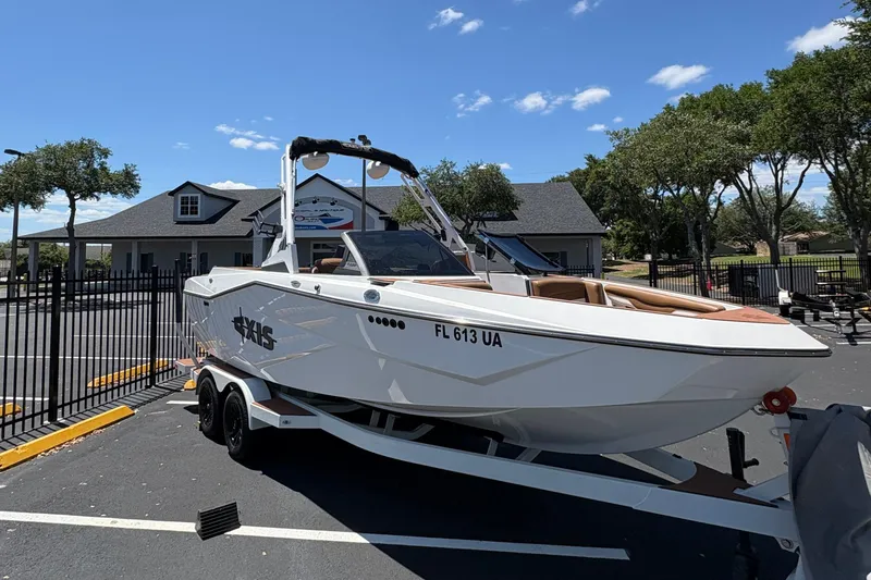 Slide: The Image of 2025 Axis T220 boat on trailer in parking lot, sunny day, trees and building in background. - 1