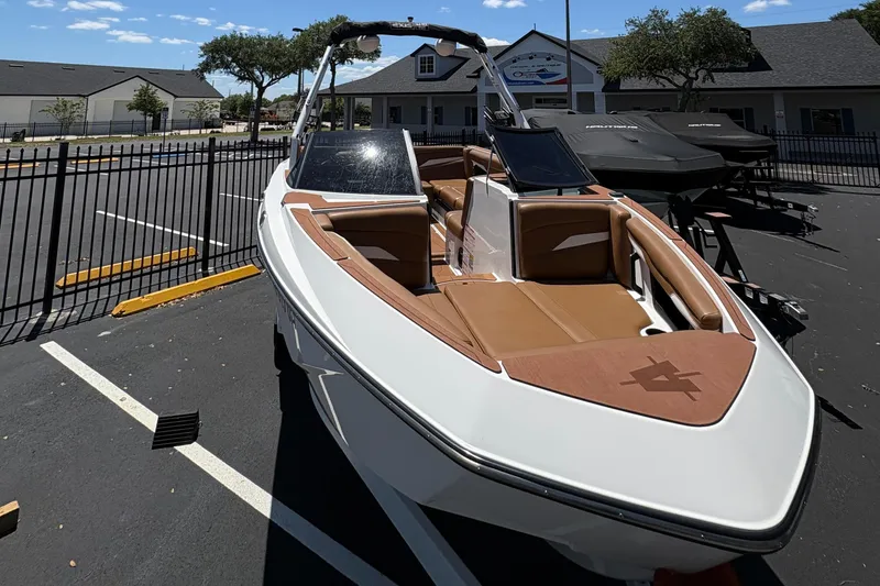 Slide: The Image of 2025 Axis T220 boat with brown interior, parked outdoors near a fence. - 2