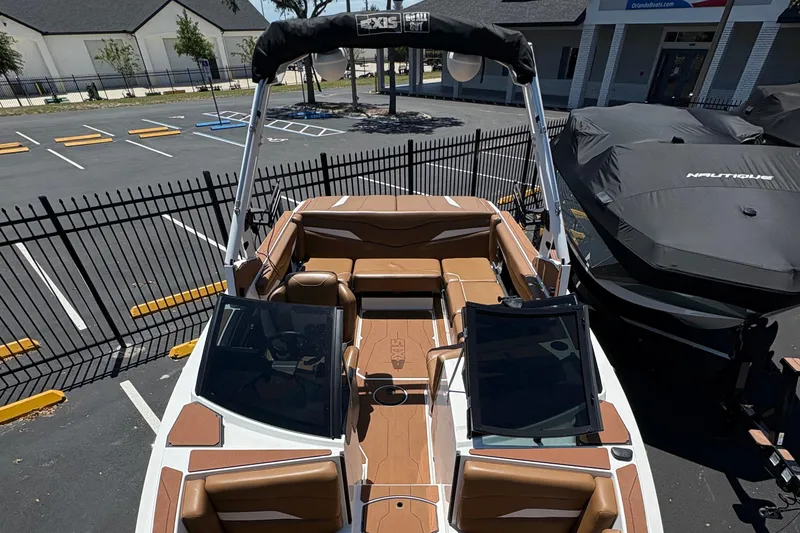 Slide: The Image of 2025 Axis T220 boat with brown interior, parked in a lot near a fence. - 4