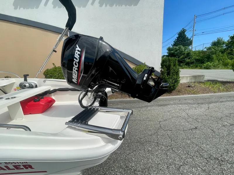 Slide: The Image of A 2027 Boston Whaler 130 Super Sport with a Mercury outboard motor, parked in a lot. - 2