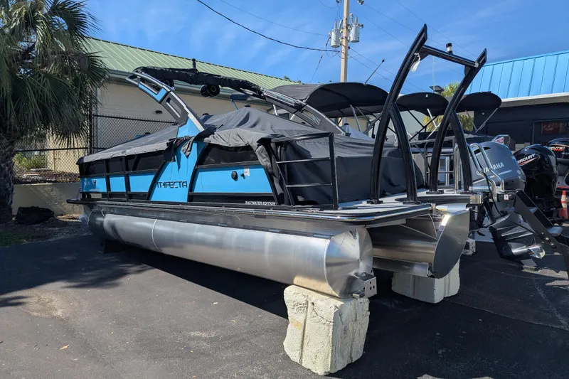 Slide: The Image of 2026 Trifecta 23SB2 SS pontoon boat with blue accents, parked outdoors. - 2