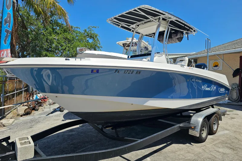 The Image of 2012 Boston Whaler 220 Outrage boat on trailer, blue and white design, parked outdoors. - 0