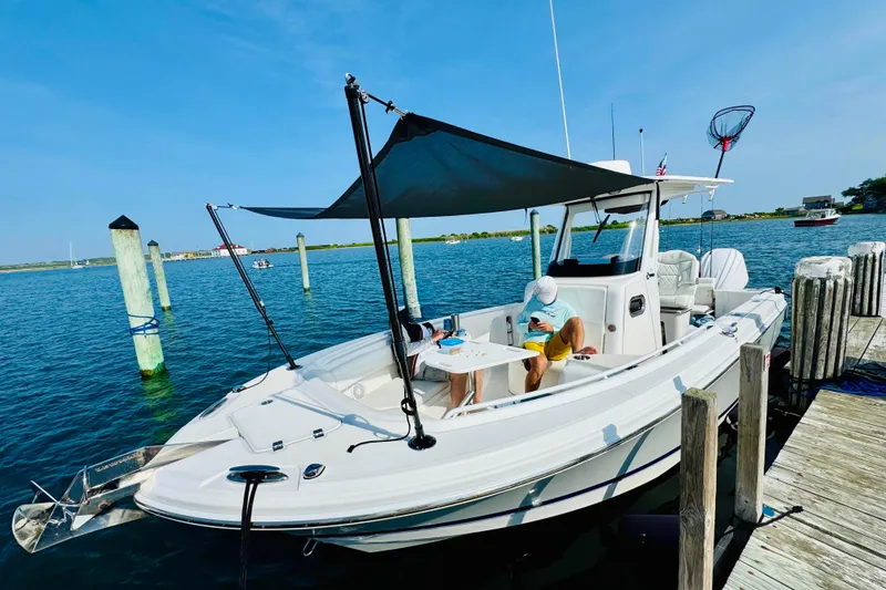 Slide: The Image of 2022 Edgewater 262CC boat docked, featuring a sunshade and a person relaxing onboard. - 4