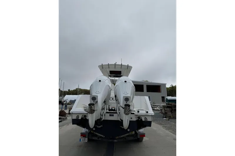 Slide: The Image of 2022 Edgewater 262CC boat with dual outboard motors, parked outdoors on a cloudy day. - 7