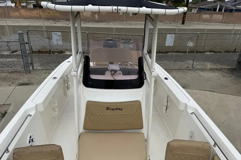 Slide: The Image of 2022 Bayliner Trophy T22CX boat with beige seating and canopy, docked near a fence. - 6