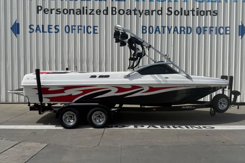 The Image of 2006 MB SPORTS B52 boat with red and white design, parked at a boatyard. - 0