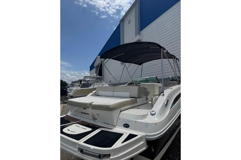 Slide: The Image of 2013 Sea Ray 280 Sundeck boat with canopy, parked outdoors near a blue and white building. - 10