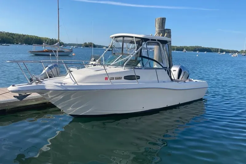 Slide: The Image of 2002 Wellcraft 24 Walkaround boat docked on a serene lake under clear blue skies. - 2