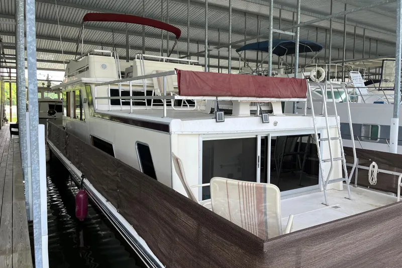 Slide: The Image of 1990 Gibson 44 houseboat docked in a covered marina, featuring a spacious deck and ladder. - 3