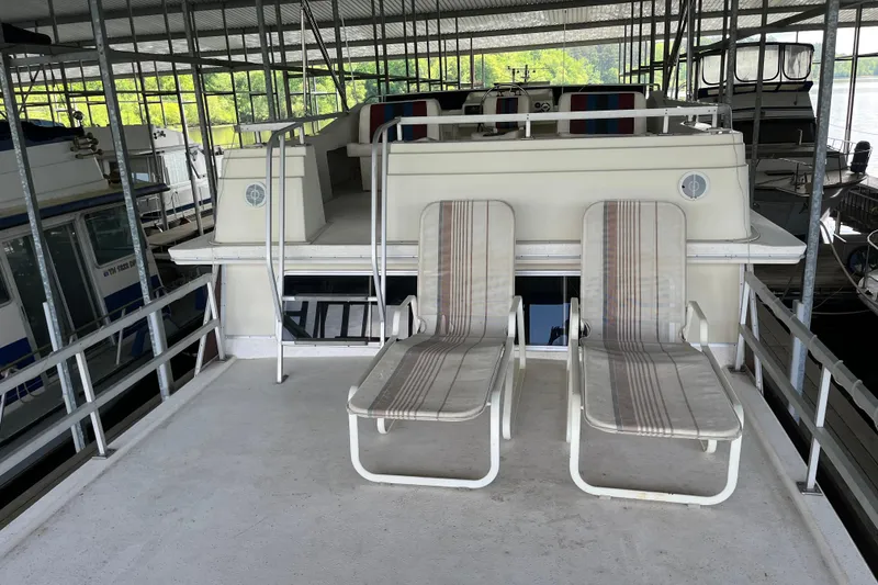 Slide: The Image of 1990 Gibson 44 houseboat with two striped lounge chairs on deck under a covered marina. - 45