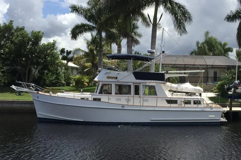 Slide: The Image of 1992 Grand Banks 46 Classic yacht docked by palm trees under cloudy sky. - 99