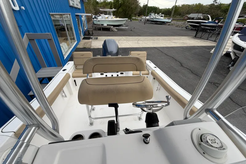 Slide: The Image of 2017 Tidewater 198 CC Adventure boat interior with seating and controls, docked near blue building. - 6