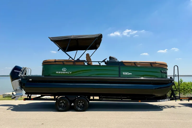 Slide: The Image of 2026 Regency 230 DL pontoon boat on trailer by a lake under blue sky. - 14