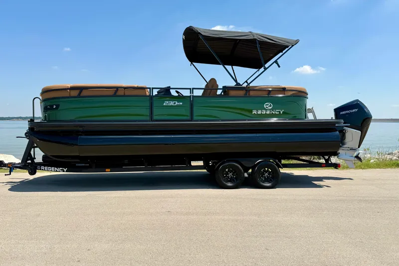 Slide: The Image of 2026 Regency 230 DL pontoon boat on trailer by a lake, featuring green and black design. - 18