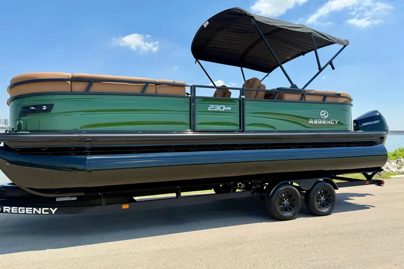 Slide: The Image of 2026 Regency 230 DL pontoon boat with canopy on trailer, parked by a lake. - 19