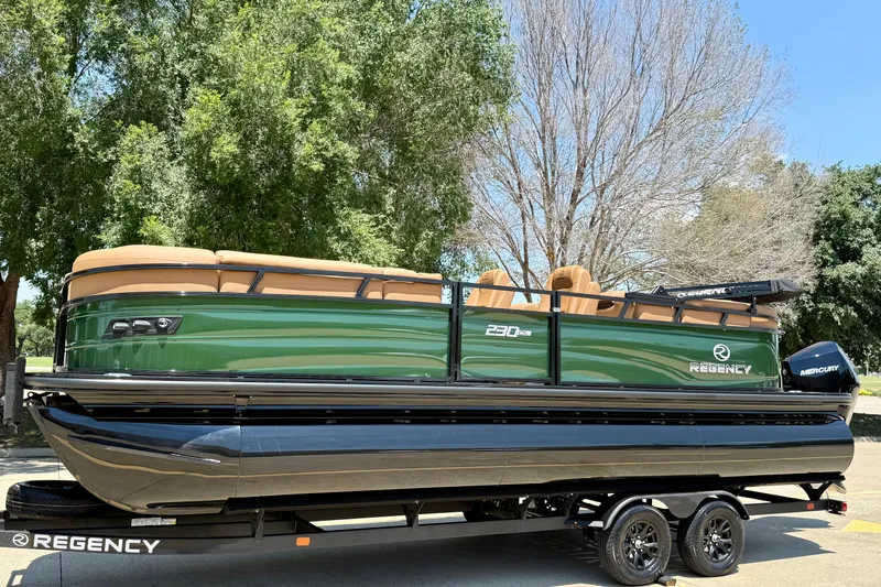 Slide: The Image of 2026 Regency 230 DL pontoon boat on trailer, green exterior, parked outdoors. - 25