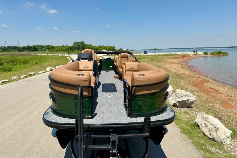 Slide: The Image of 2026 Regency 230 DL pontoon boat on lakeside road, featuring tan seating and green exterior. - 6