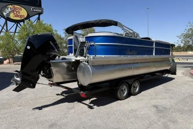 Slide: The Image of 2026 Sun Tracker Party Barge 24 XP3 pontoon boat on trailer, parked near Bass Pro Shops. - 2
