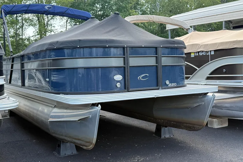 The Image of 2022 Crest Classic DLX 220 SLS pontoon boat with blue cover, parked on a trailer. - 0