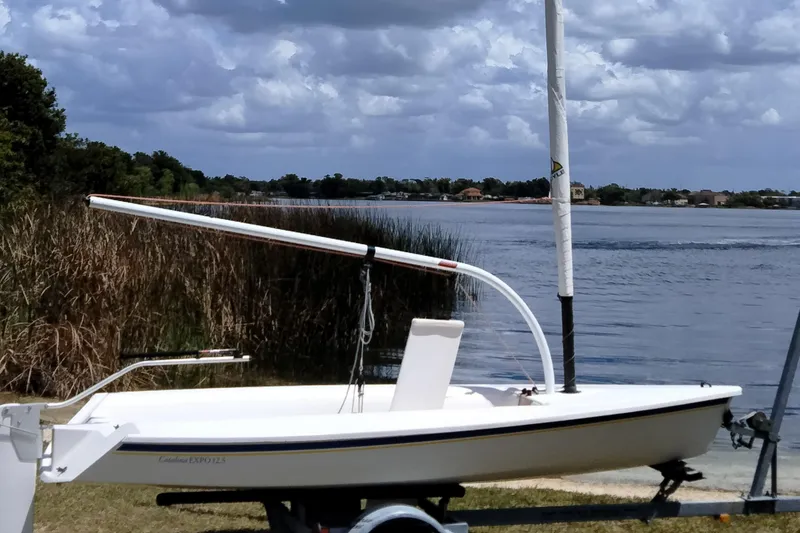 Slide: The Image of 2014 Catalina 12.5 Expo sailboat by a serene lake under cloudy skies. - 5