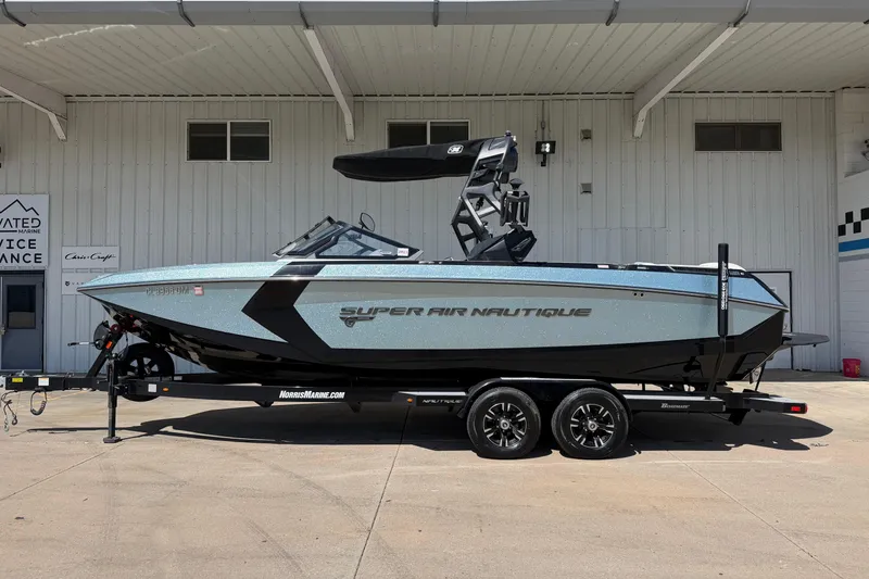 The Image of 2020 Nautique Super Air Nautique G25 boat on trailer, parked outside a service building. - 1
