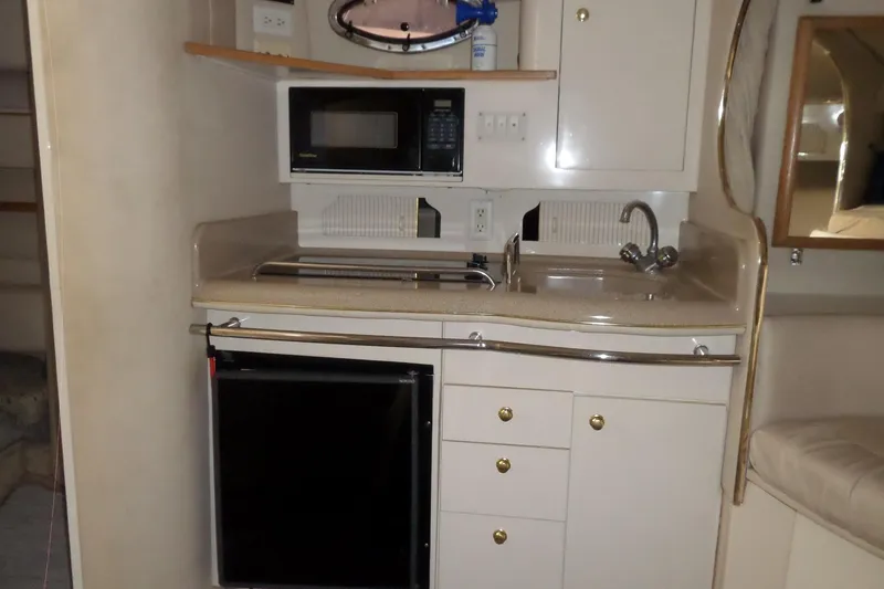 Slide: The Image of Compact kitchen area in a 1997 Sea Ray 290 Sundancer boat, featuring a microwave and sink. - 29