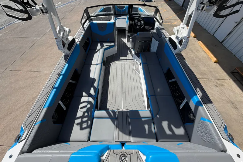 Slide: The Image of 2025 Nautique Super Air Nautique GS24 interior with blue and gray seating, docked outdoors. - 11