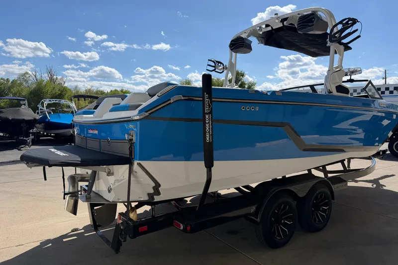 Slide: The Image of 2025 Nautique Super Air Nautique GS24 boat in blue, parked on a trailer under a sunny sky. - 6