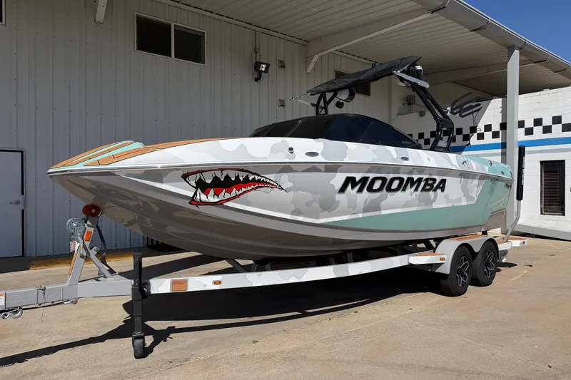 Slide: The Image of 2025 Moomba Mojo boat with shark mouth design on trailer, parked outside a building. - 2